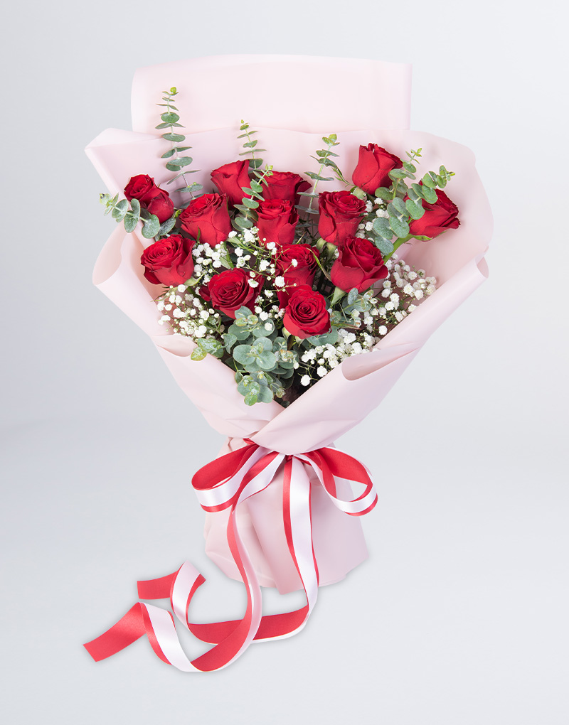 ช่อดอกกุหลาบสีแดง 13 ดอก ห่อด้วยกระดาษสีชมพู ผูกริบบิ้นสีขาวและสีแดง