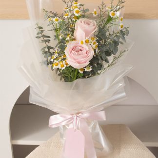 ช่อดอกกุหลาบสีชมพู 2 ดอก ช่อเล็ก แซมดอกเดซี่และยูคาลิปตัสใบกลม ห่อกระดาษใส ขึ้นเงา ดูไร้เดียงสา